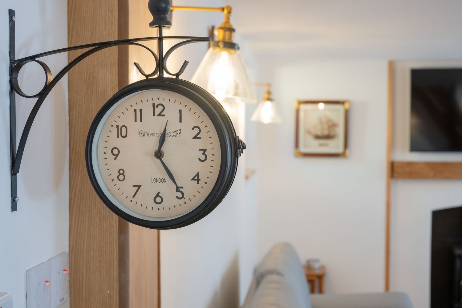 Vintage-style train station clock mounted on a wall with pendant lighting in the background.