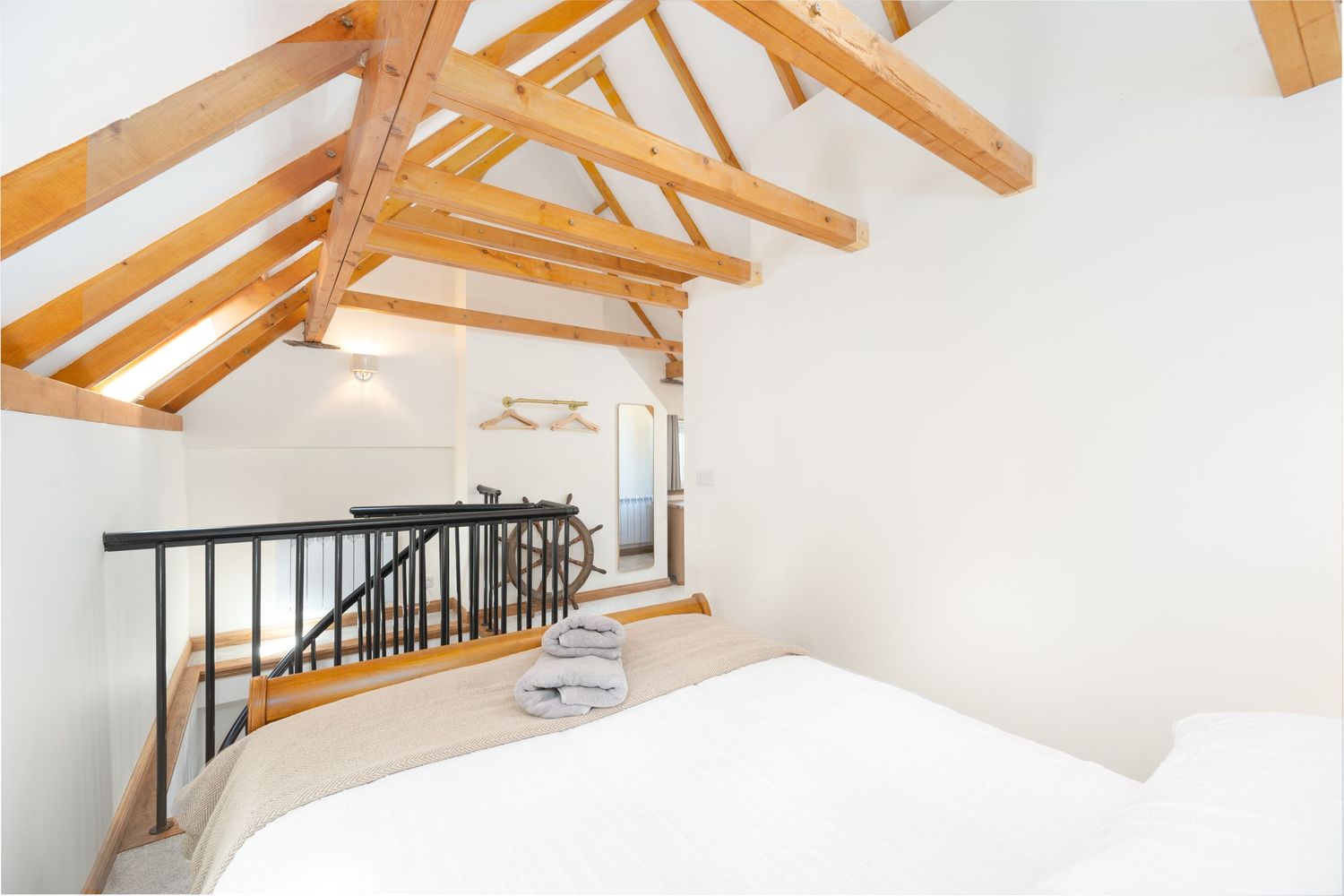 Cozy loft bedroom with exposed wood beam ceiling, white walls, and black metal railing overlooking lower level.