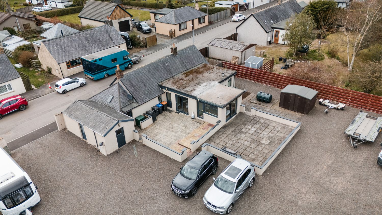 Aerial drone view of a commercial building with multiple cars parked in the lot and gray rooftops.