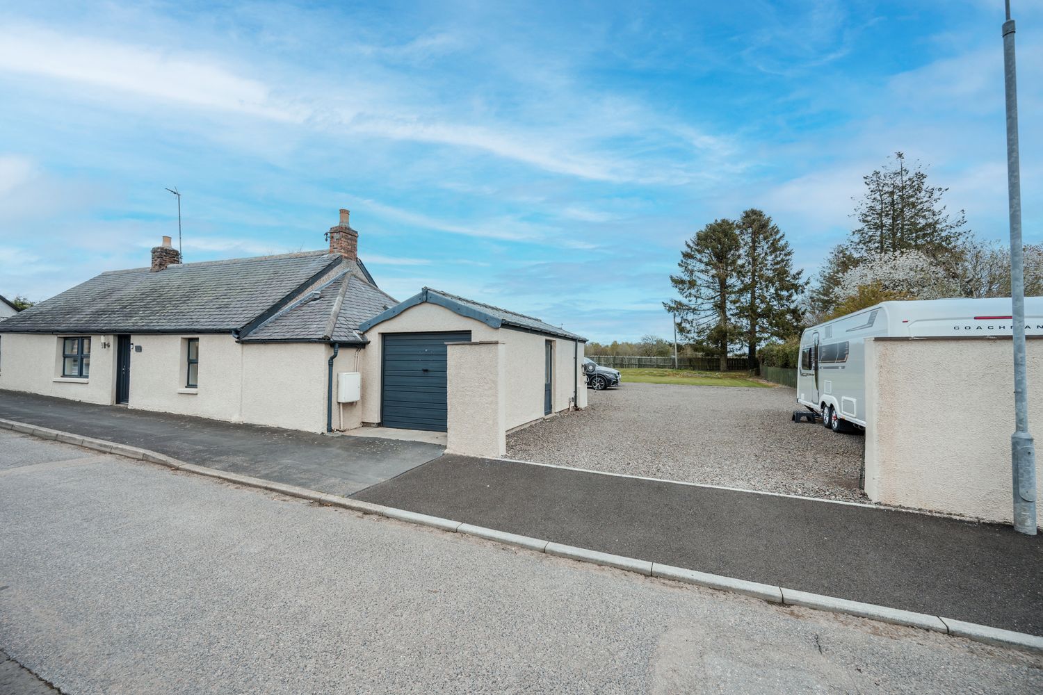Single story gray and white bungalow with blue garage door and driveway under bright blue sky.