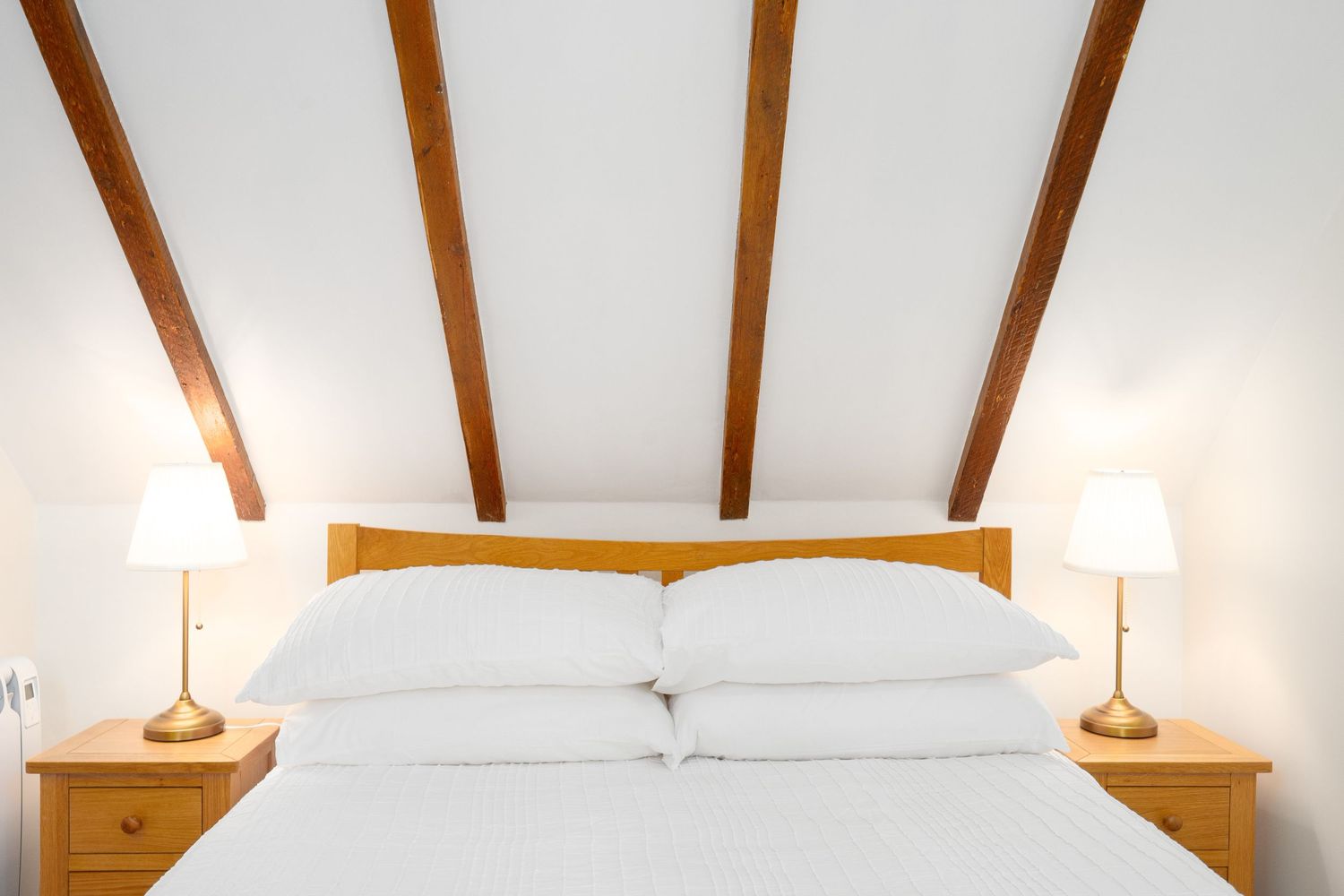 Modern bedroom with exposed wooden ceiling beams, white walls, and matching bedside tables with lamps.