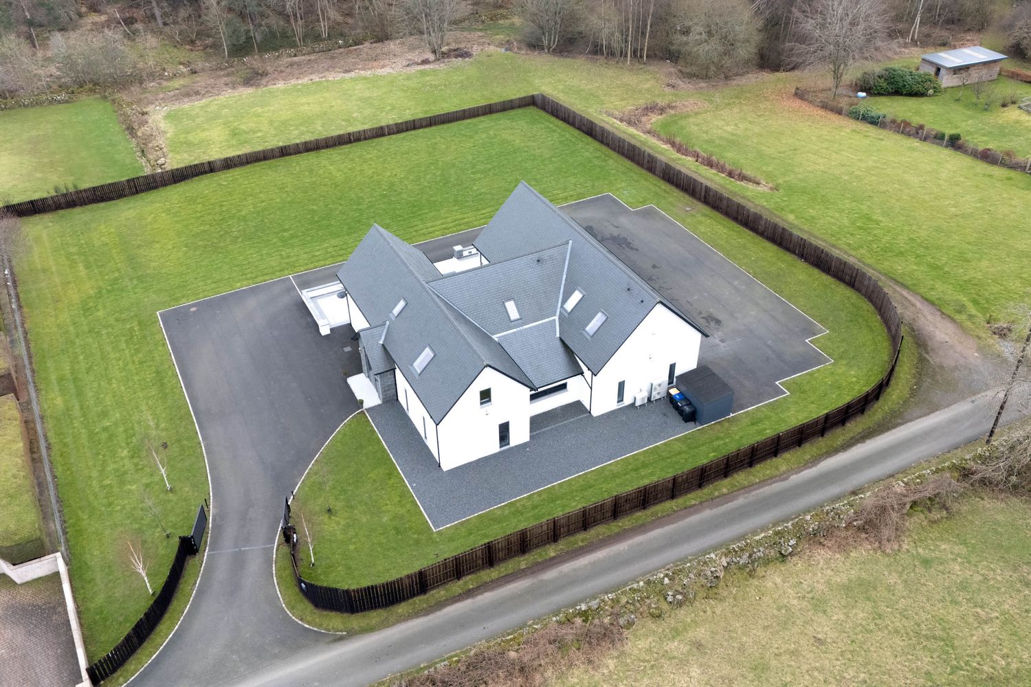Drone shot showing a residential property with curved driveway and landscaped gardens viewed from above.