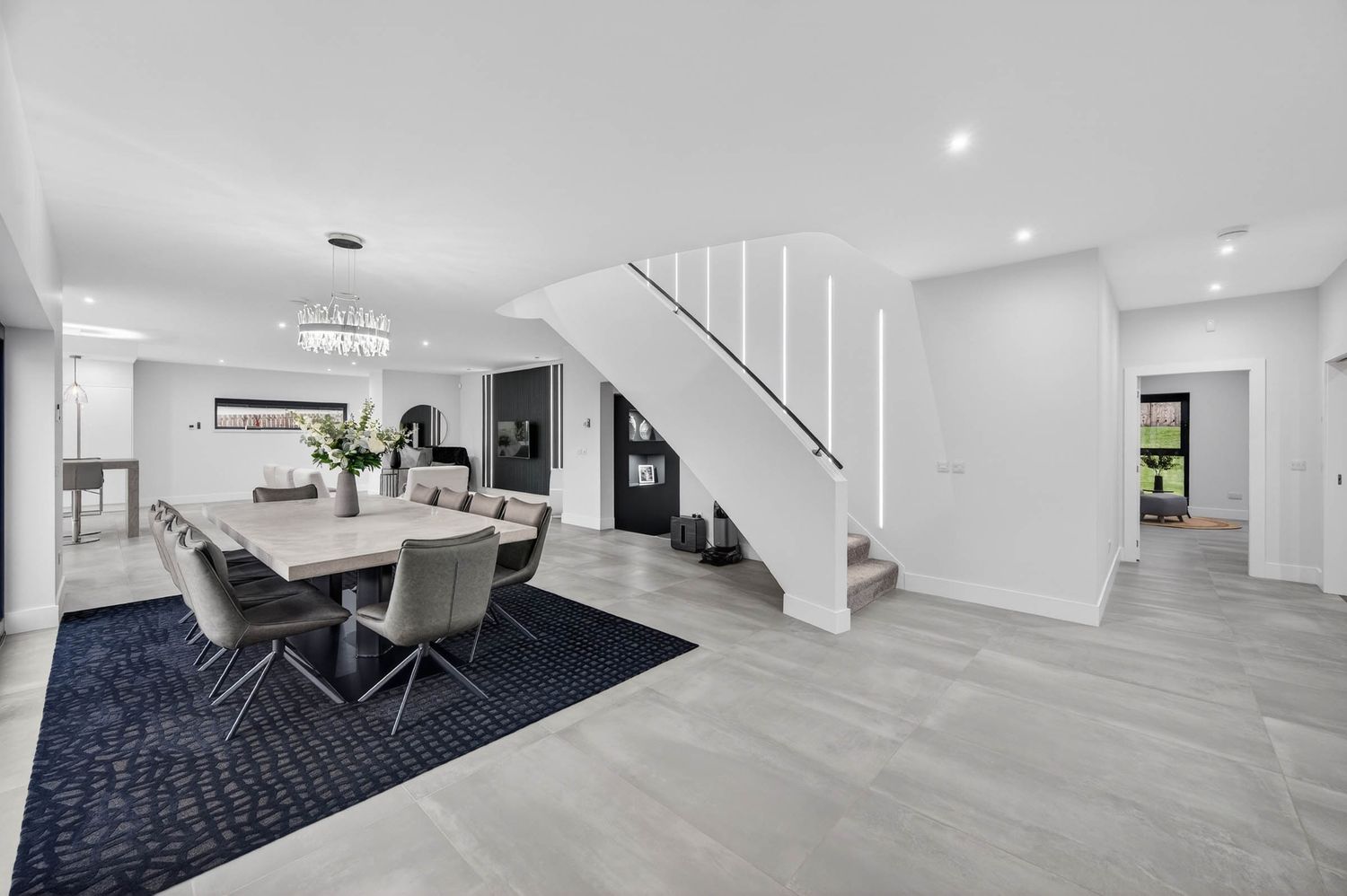 Modern white and gray basement renovation with navy carpet, recessed lighting, and staircase leading upstairs.