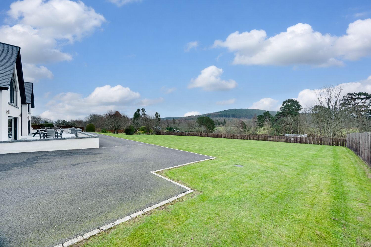 Race track with green grass and white safety barriers winding through a scenic countryside on a sunny day.