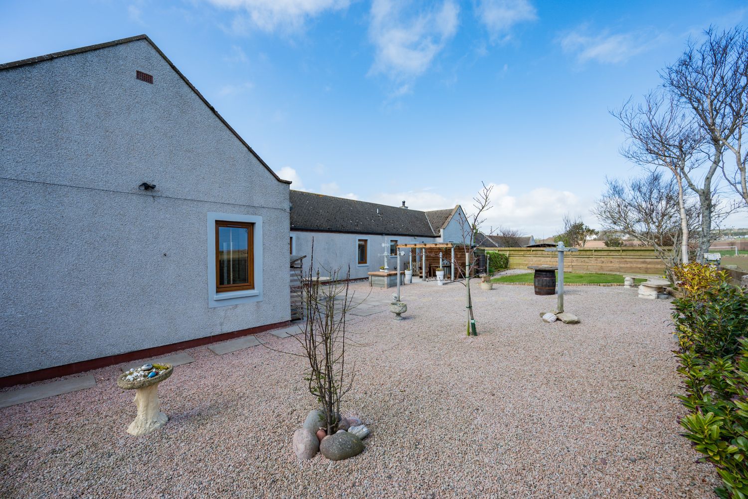 Modern white cottage-style house with gravel driveway and landscaped garden set against a bright blue sky.