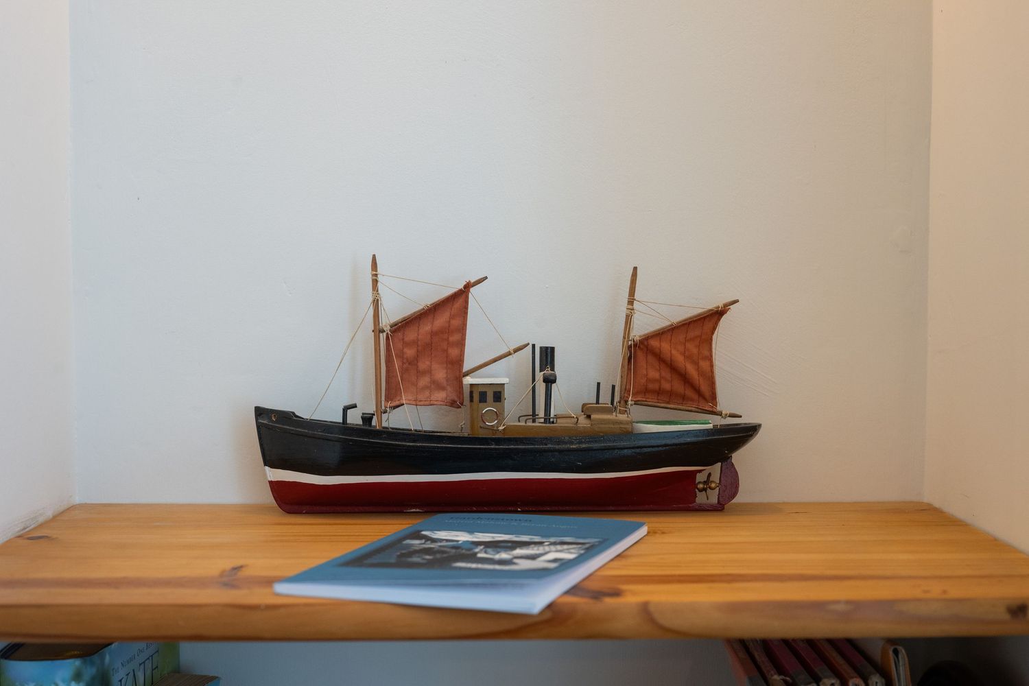 Model ship with red sails displayed on wooden table with nautical artwork.