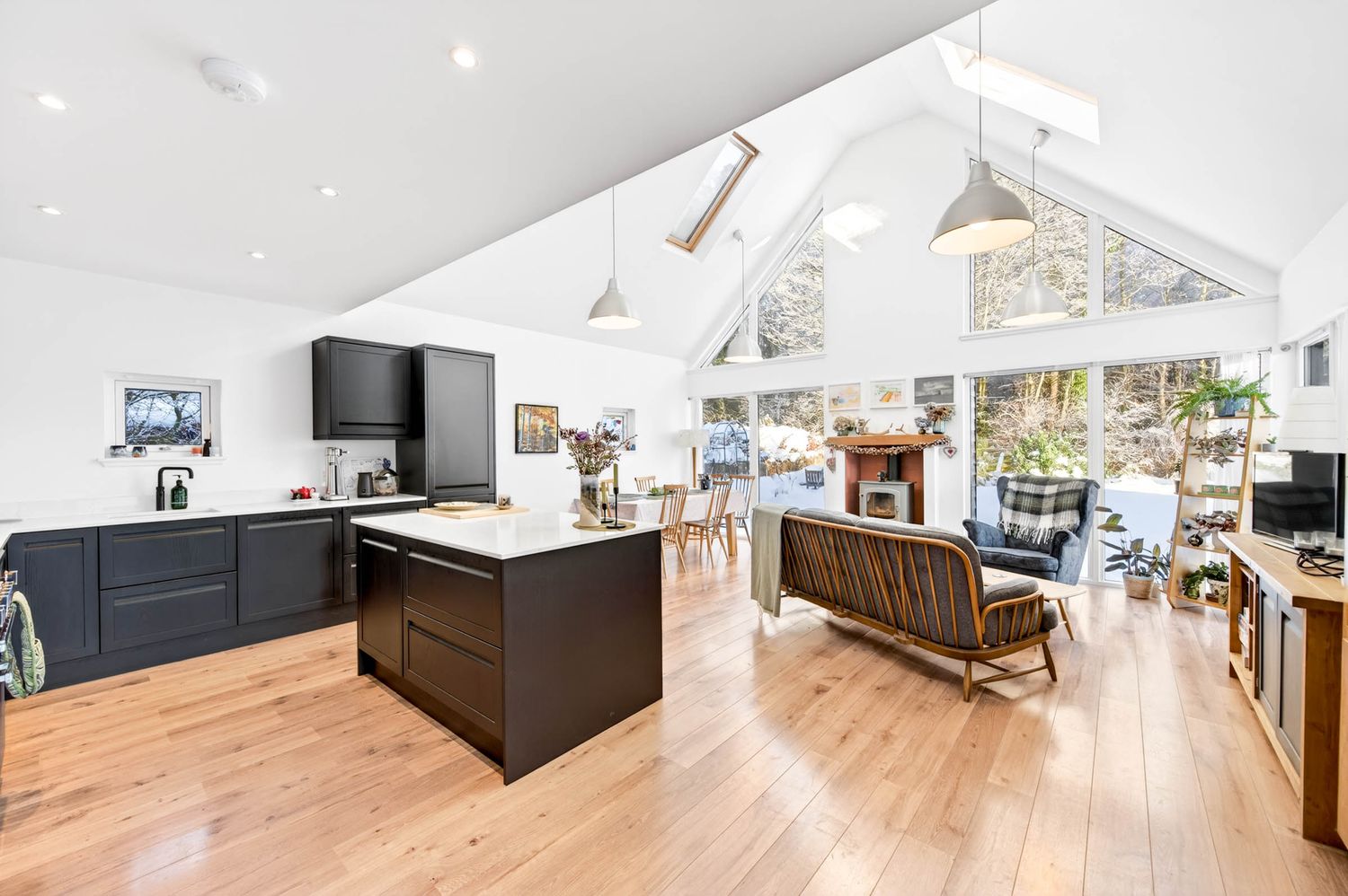 Bright open-plan living space with vaulted ceilings, hardwood floors, and large windows offering natural light.