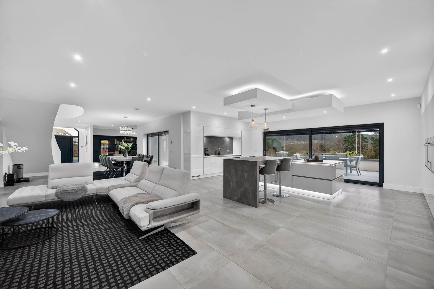 Modern luxury living room with gray flooring, black rug, white sectional sofa and contemporary lighting fixtures.