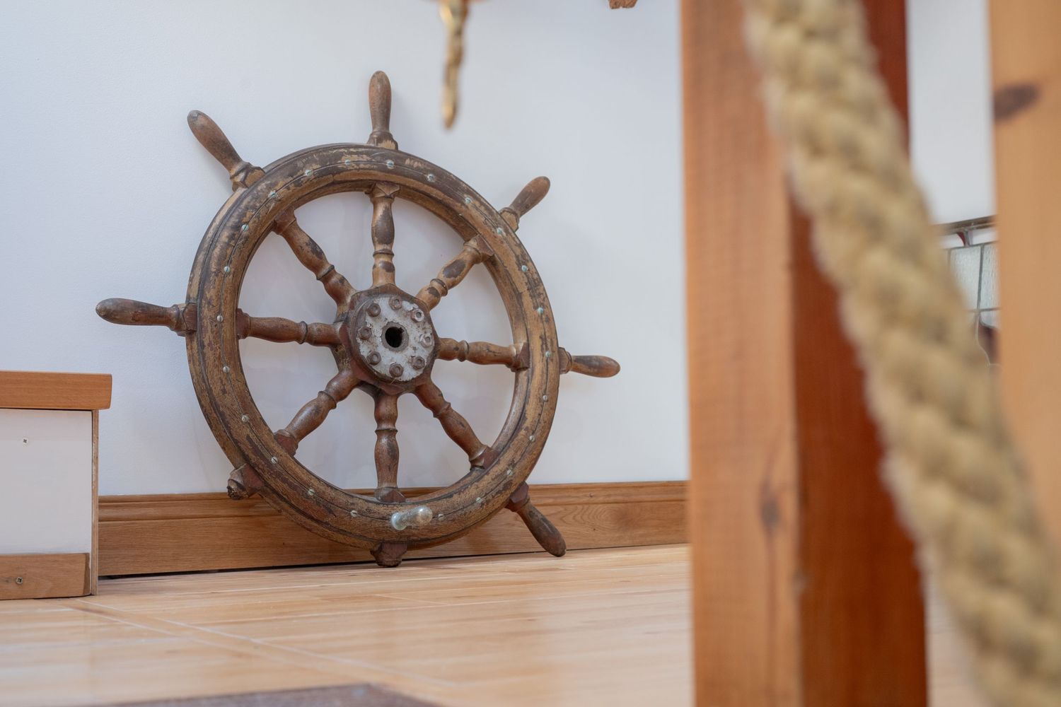 Vintage wooden ship's wheel mounted on wall with rope decoration.
