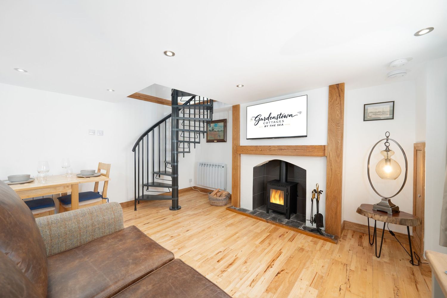 Living room with spiral staircase, wooden floors and black fireplace under white ceiling.
