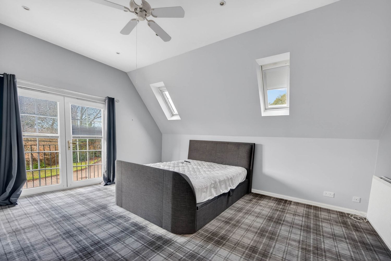 Large master bedroom with vaulted ceiling, ceiling fan, and plaid carpet flooring.