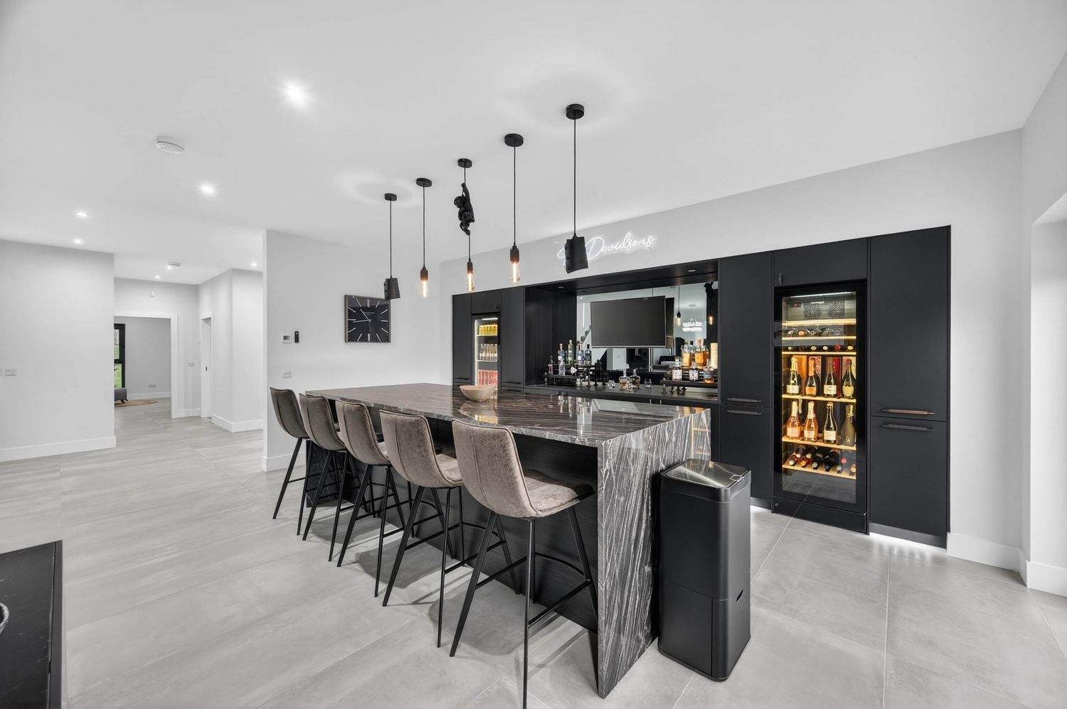 Modern home bar with black accent wall features pendant lights and gray barstools along a sleek counter.