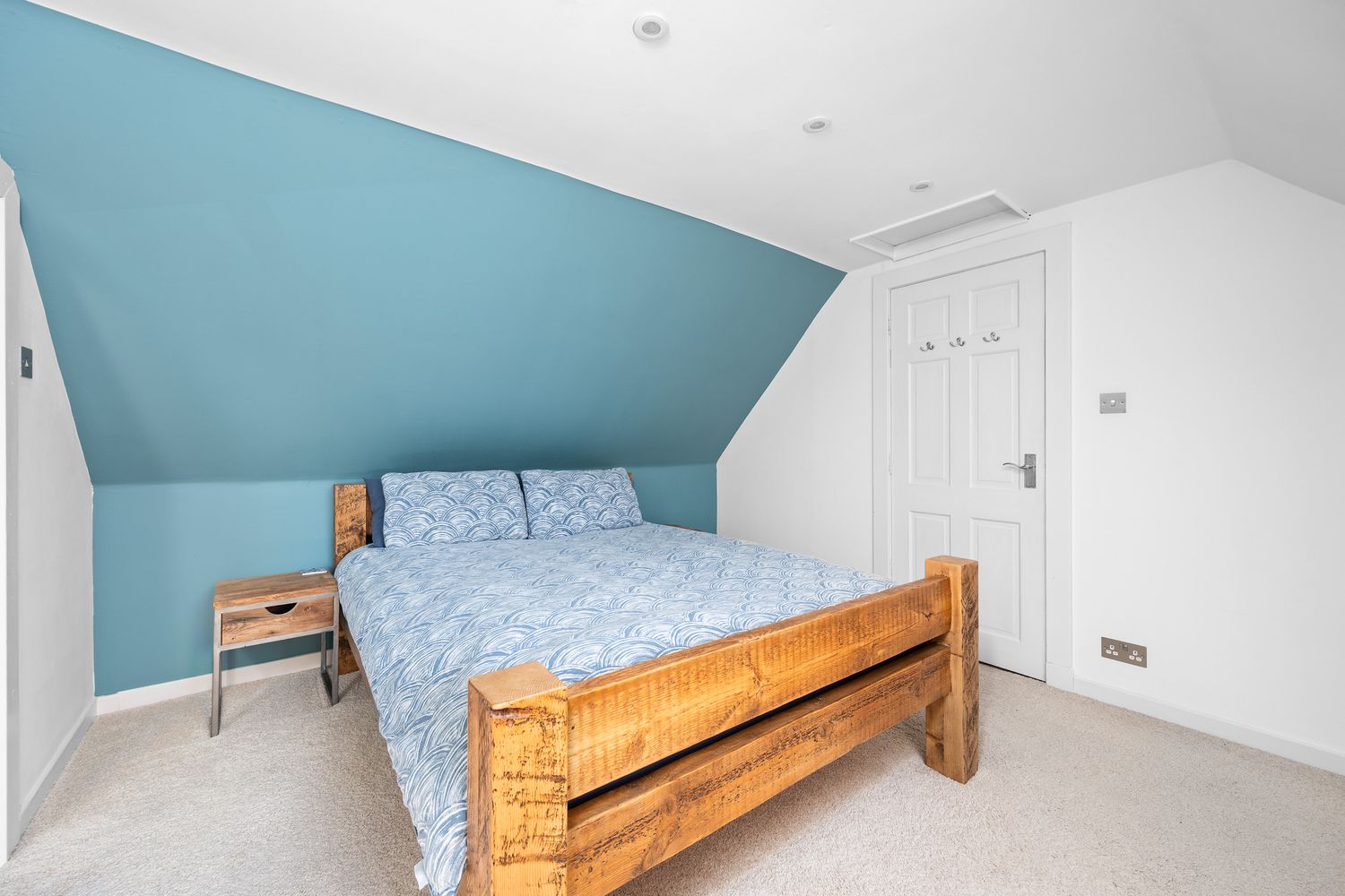 Modern attic bedroom with light blue walls, wooden bed frame and white trim in a bright sloping space.