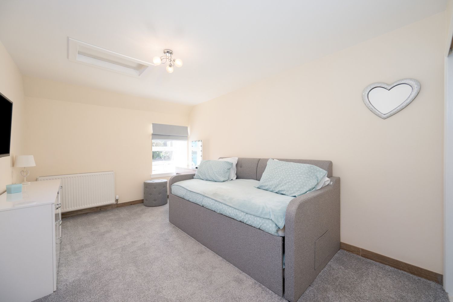 Modern bedroom interior with gray daybed, heart wall decor, and bright decor in soft blue and white color scheme.
