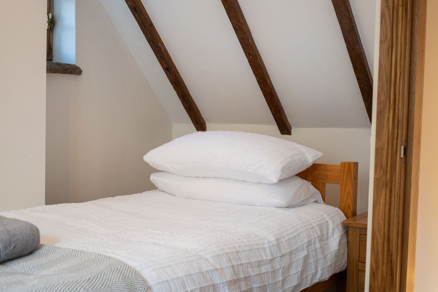 Cozy attic bedroom with exposed wooden beams and fresh white linens on single bed.