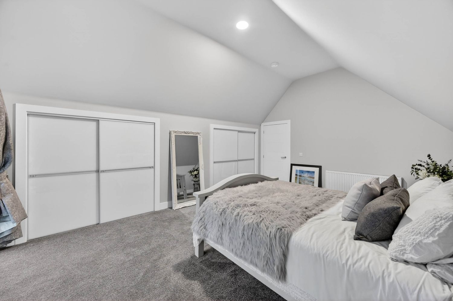 Modern attic bedroom with white vaulted ceiling, gray carpet, and built-in closets features a cozy bed with plush bedding.