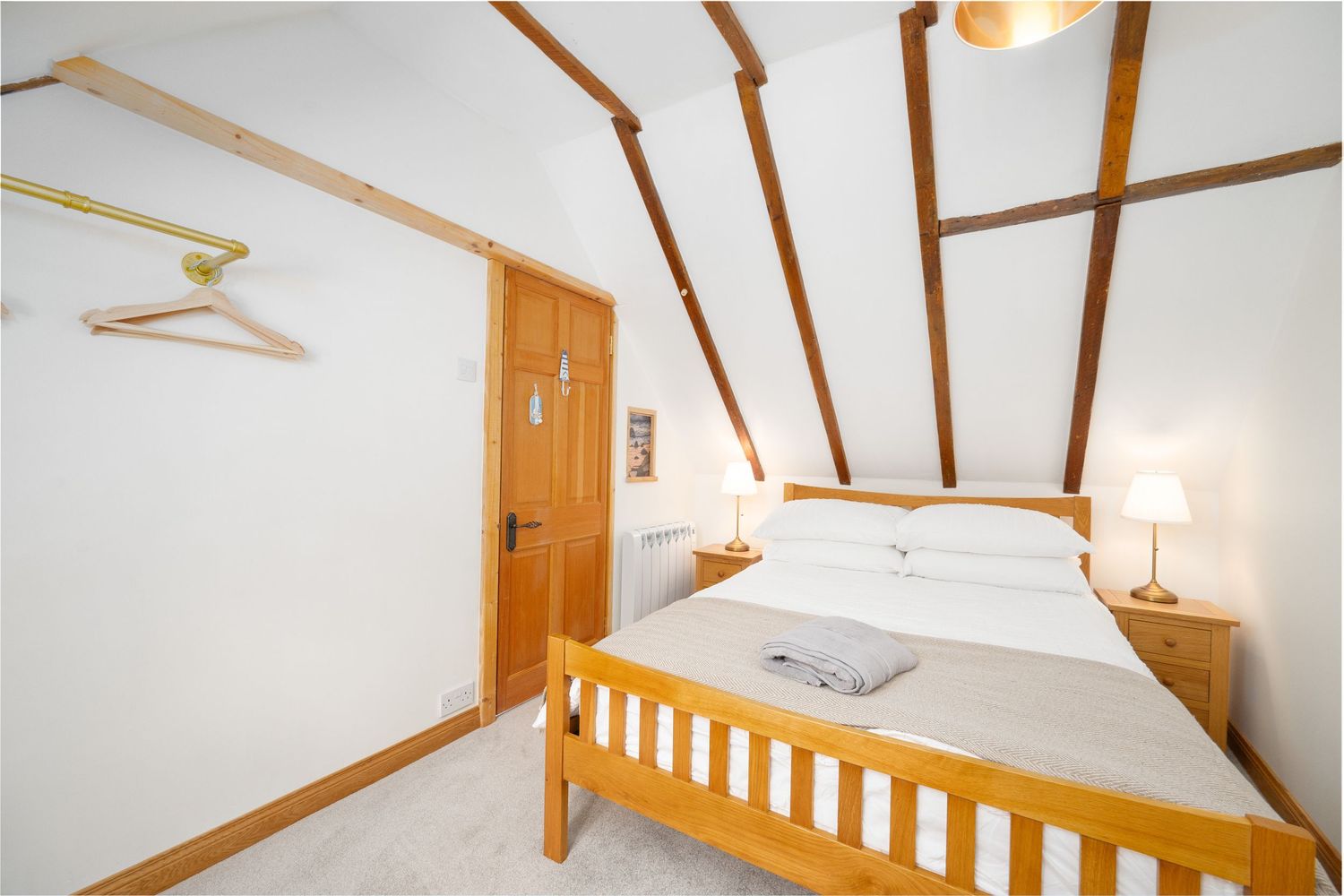 Cozy bedroom with white walls, wooden ceiling beams, and a pine bed frame with crisp white bedding.