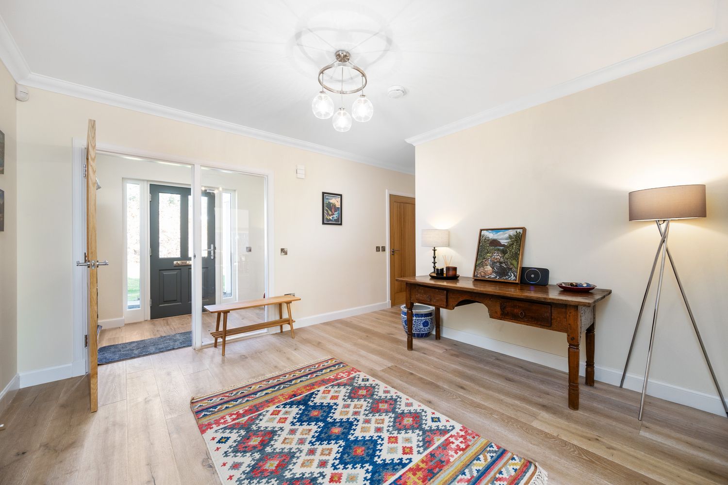 Modern entry foyer with wooden desk, decorative rug, bench, and stylish floor lamp in a bright home interior.