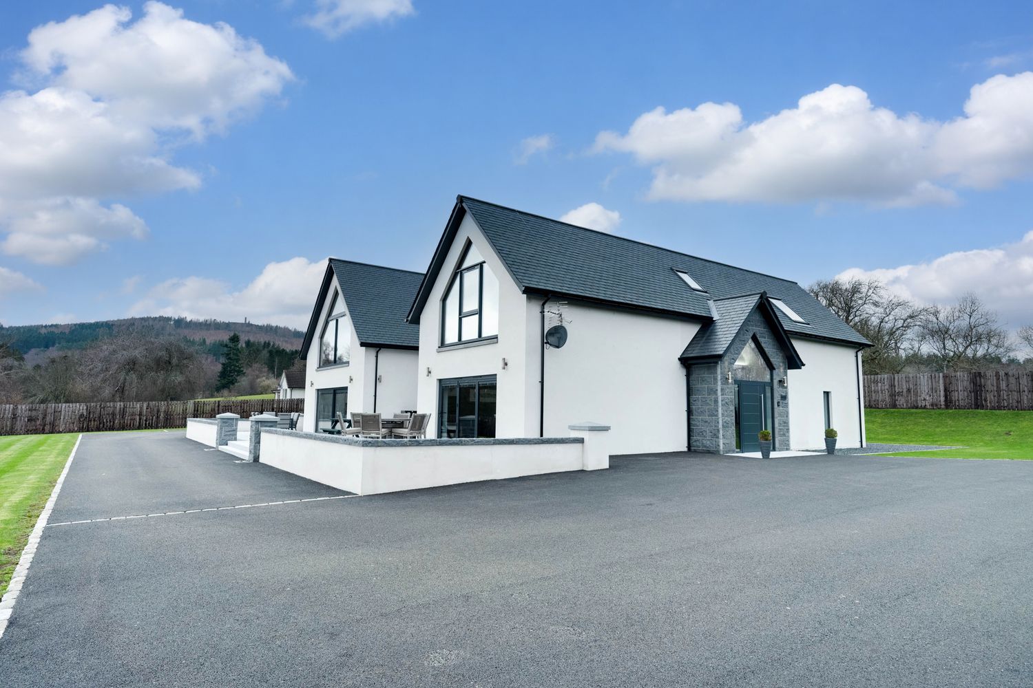 Modern white buildings with sloped roofs sit against a blue sky with rolling green hills in the countryside.