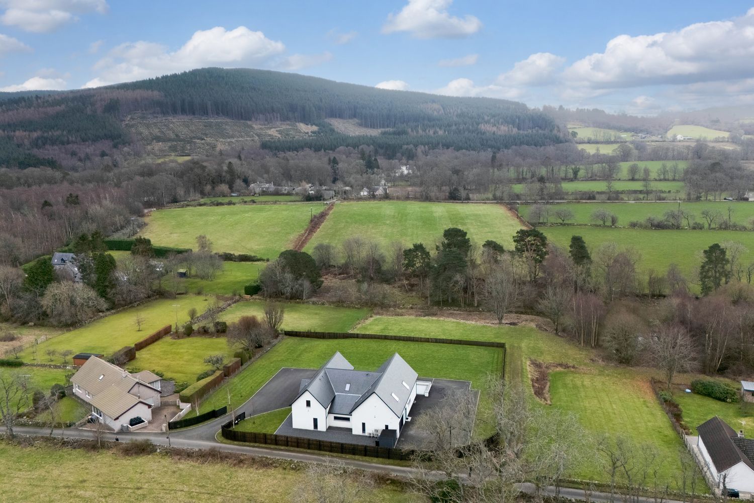 Sweeping vista of pastoral farmland showing white houses nestled among green fields with mountains in the background.