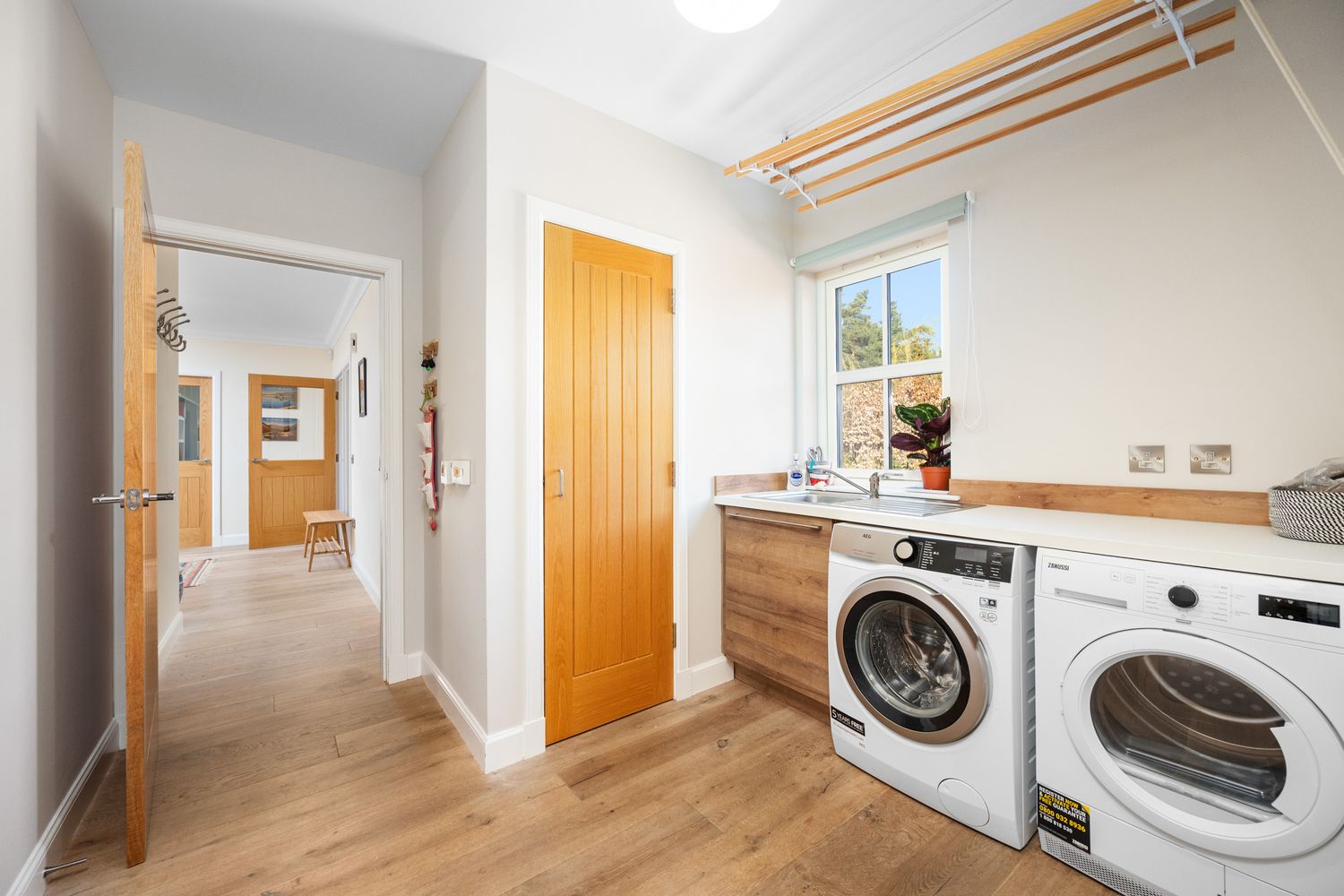 Bright utility room with wooden door, white walls, and side-by-side washer and dryer units under white countertop.