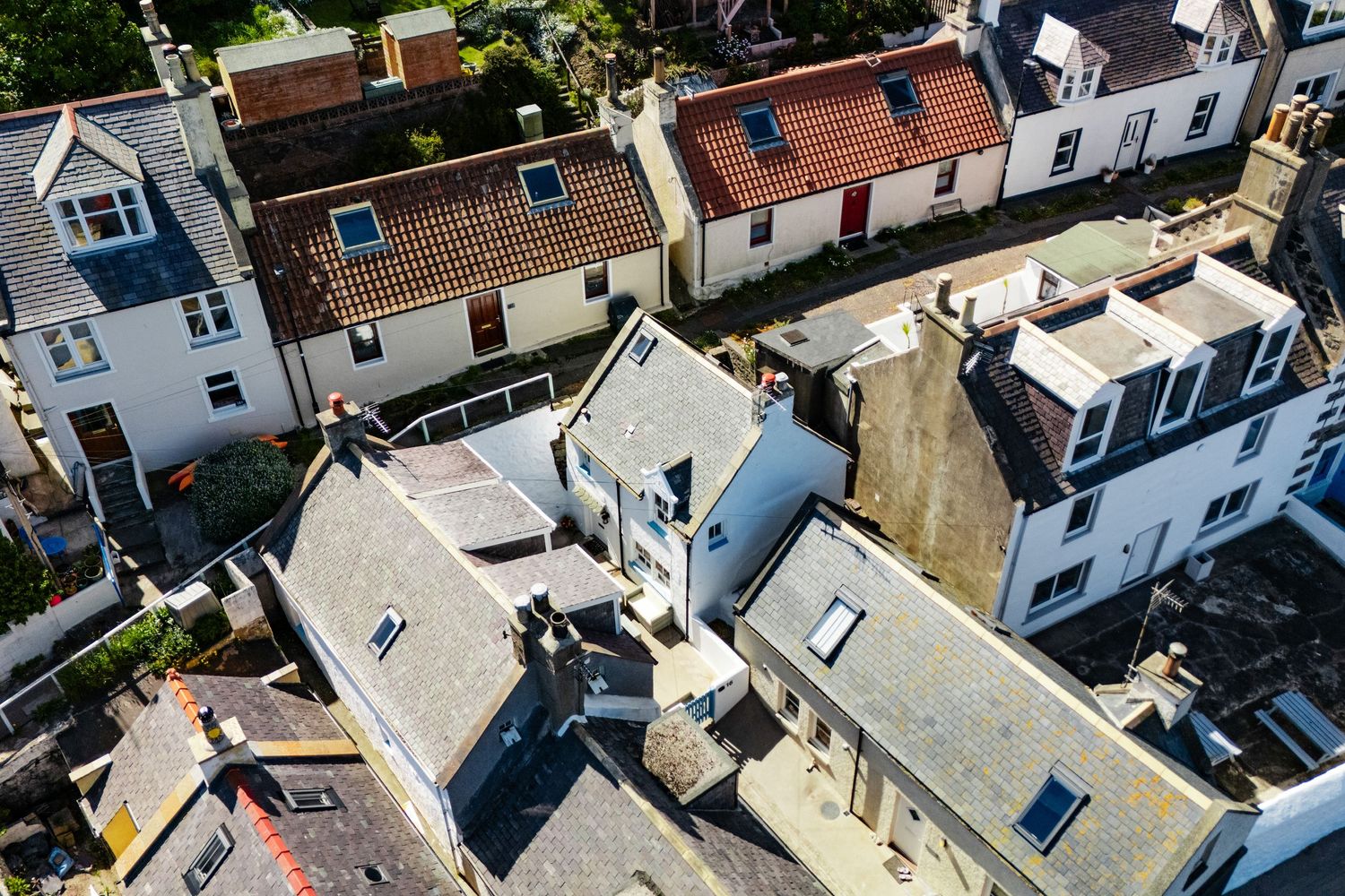 Aerial view of traditional cottage rooftops in a seaside neighborhood with white and gray buildings.