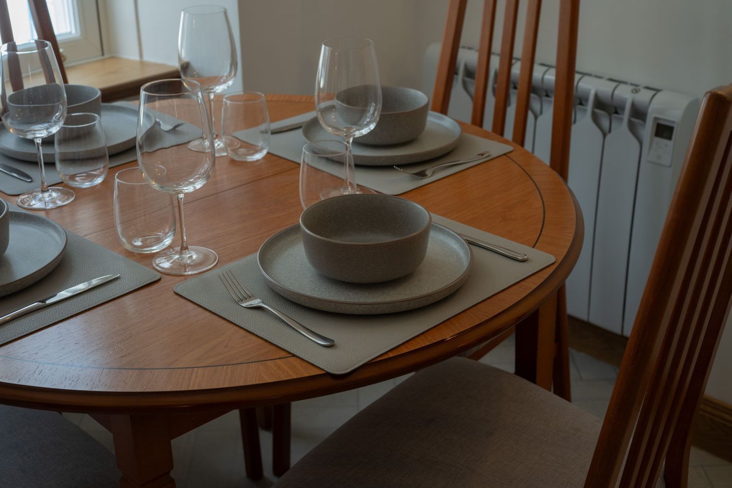 Elegant dining table setting with wine glasses and gray plates on a wooden round table.