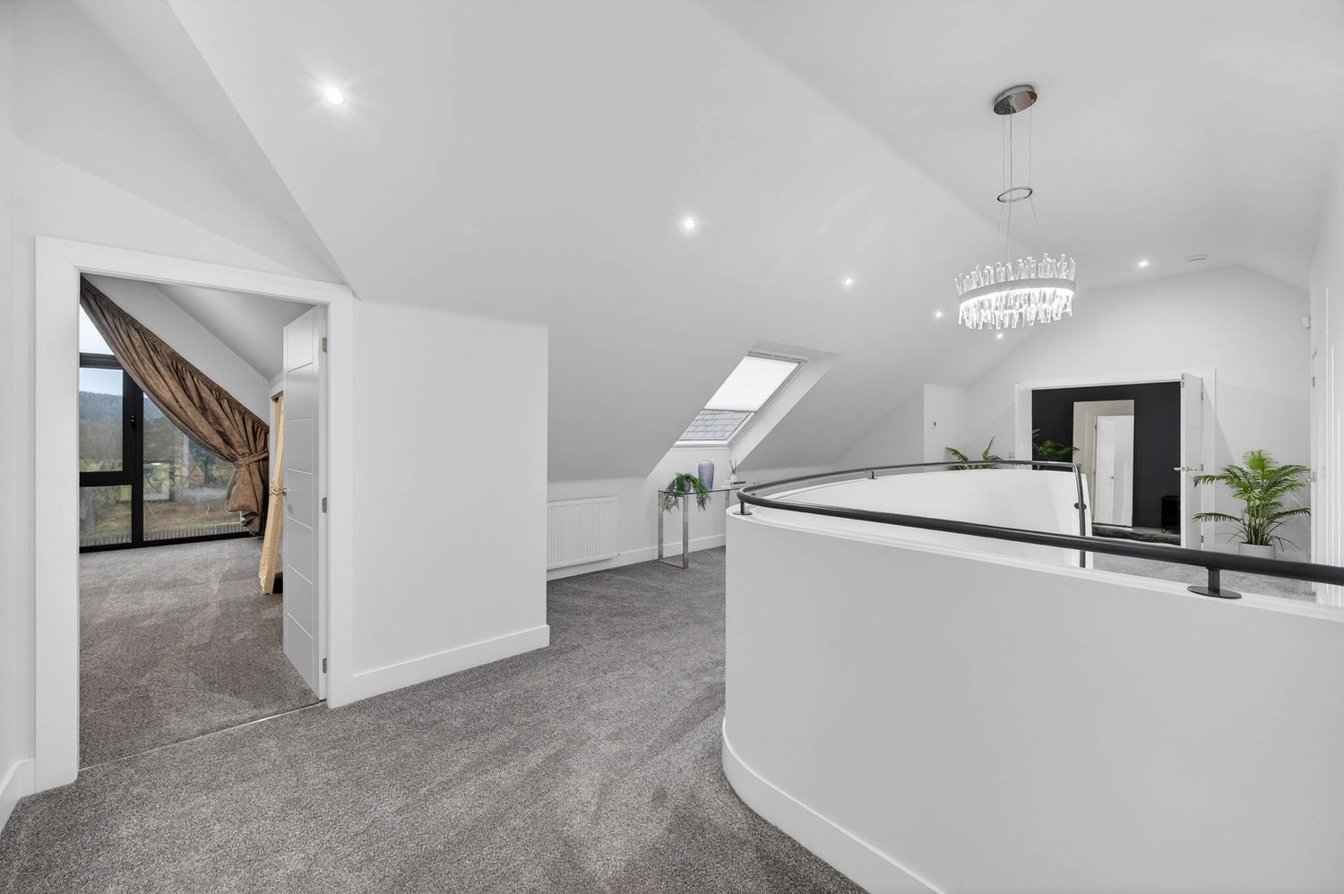 Modern attic conversion with white walls, grey carpet, recessed lighting and curved balustrade in a contemporary home.