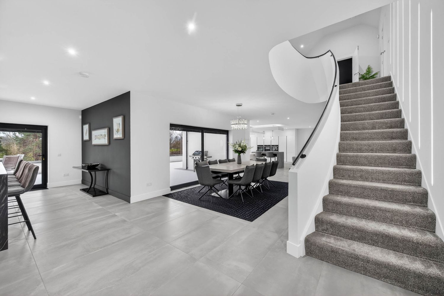 Modern interior hallway with carpeted stairs, white walls, and recessed lighting leading to upper level.