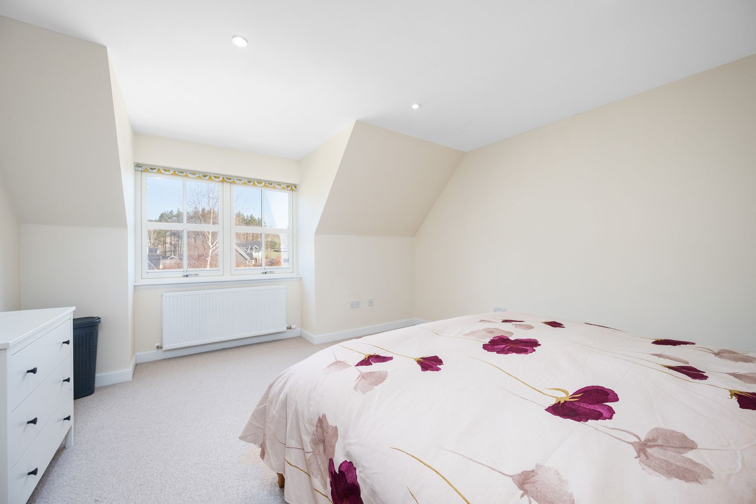 Bright loft bedroom with carpeted floor, white walls, large window, and floral bedding on double bed.