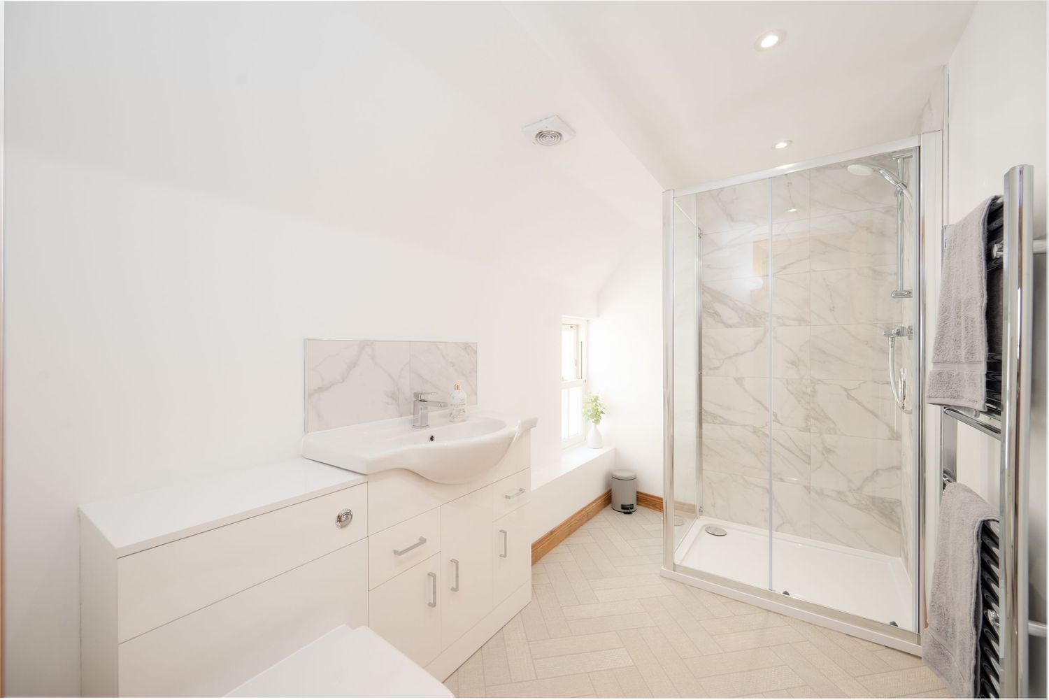 Modern white bathroom interior with marble shower enclosure, floating vanity cabinet and heated towel rail.