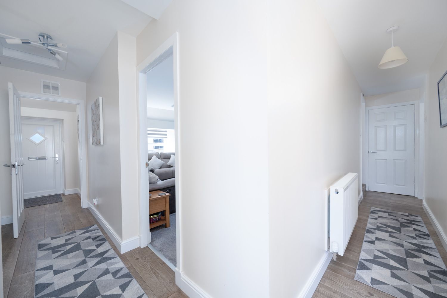 Modern white hallway interior with geometric patterned flooring and radiator along the wall.