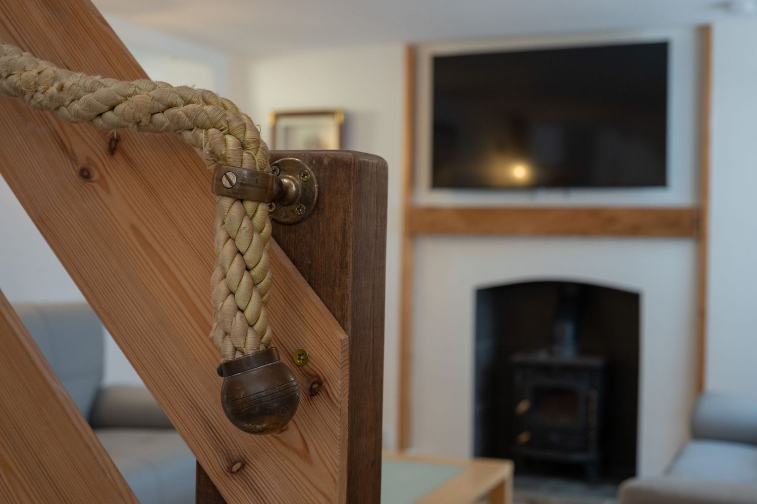Wooden staircase banister with rope railing detail in a cozy room featuring a wood stove and TV mounted above.