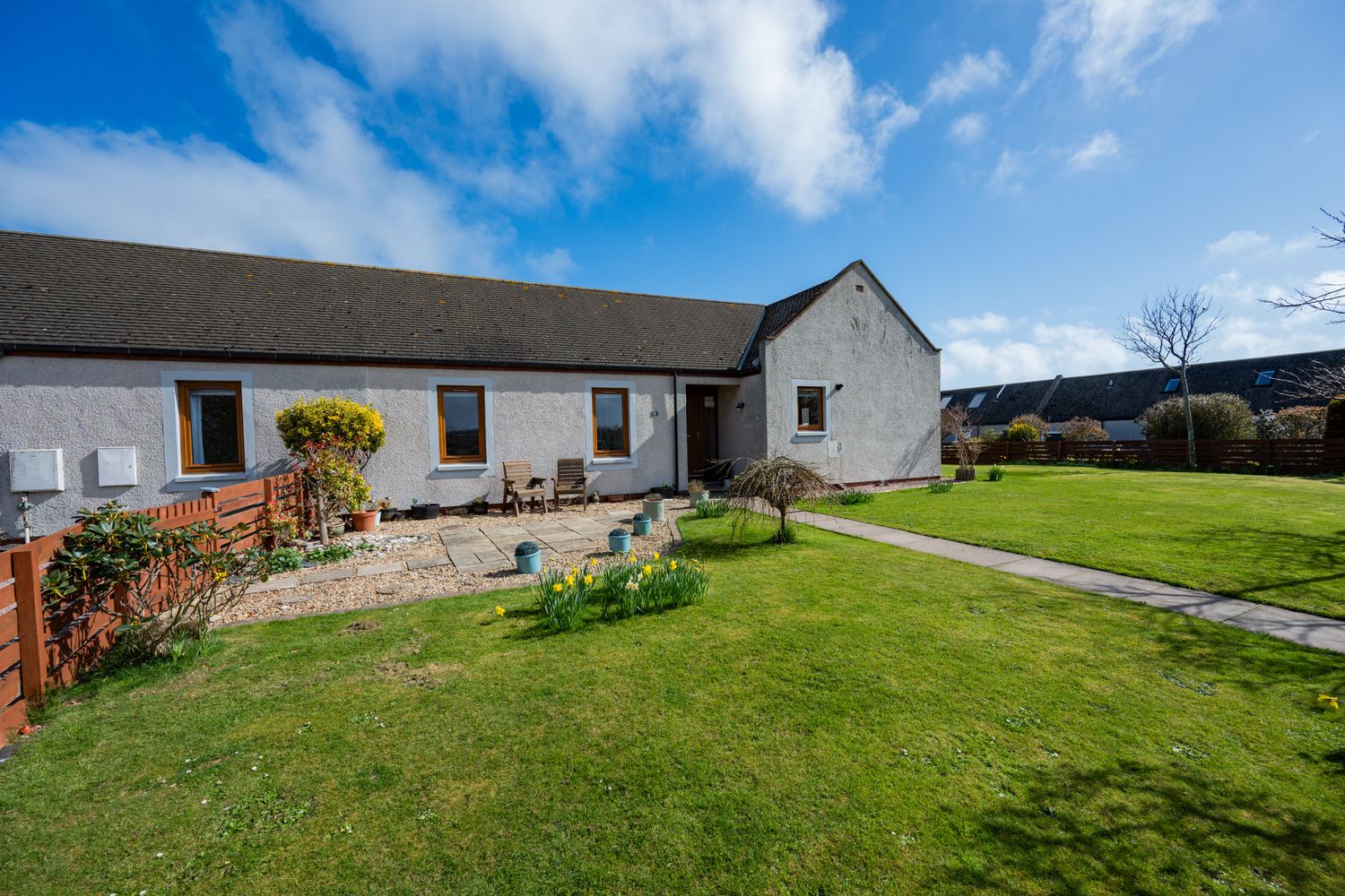 Single story white cottage-style house with well-maintained lawn and garden against bright blue sky.