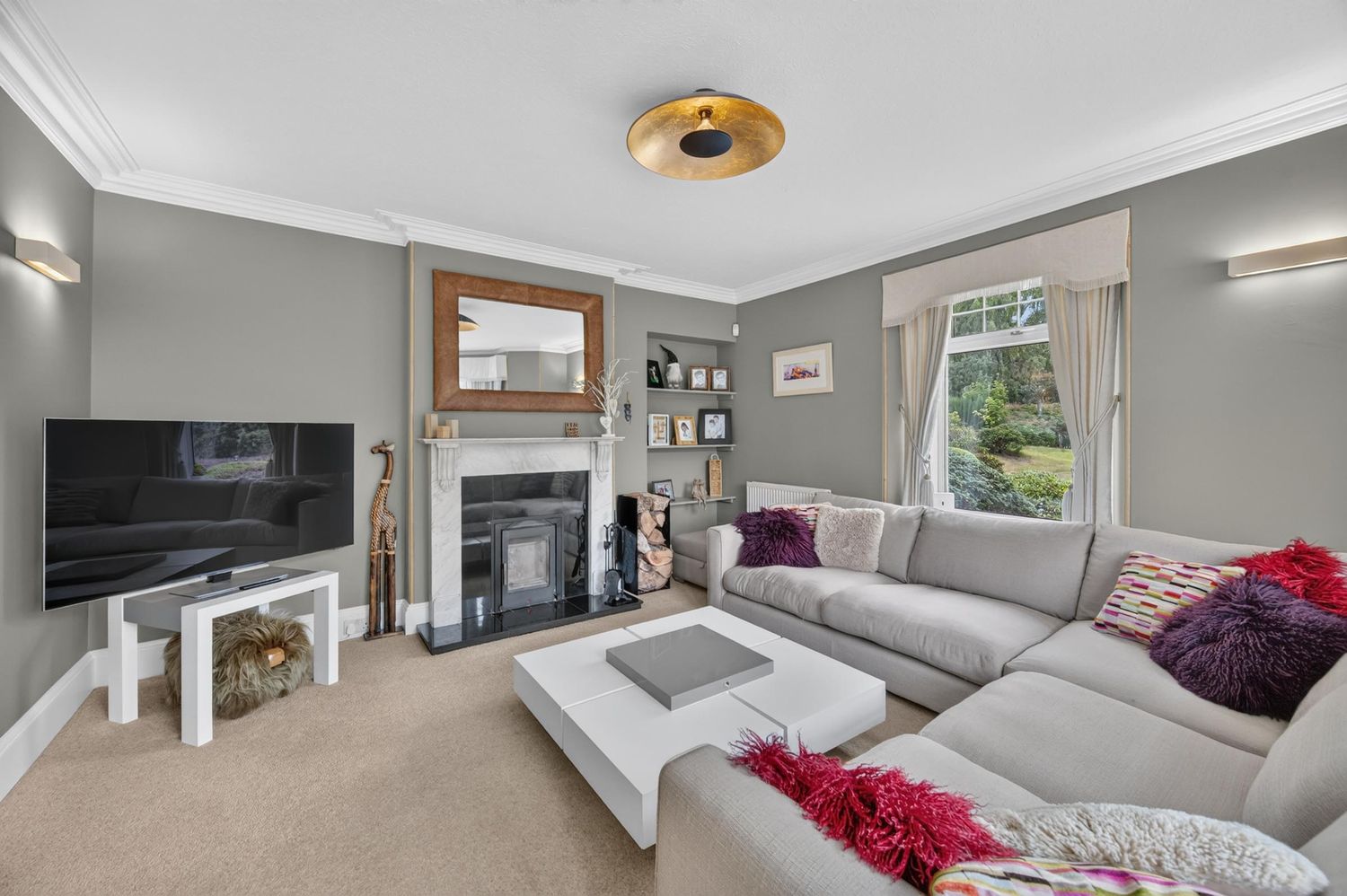 Elegant living room with grey walls, large corner sofa, white coffee table, fireplace, and bright window with garden views.