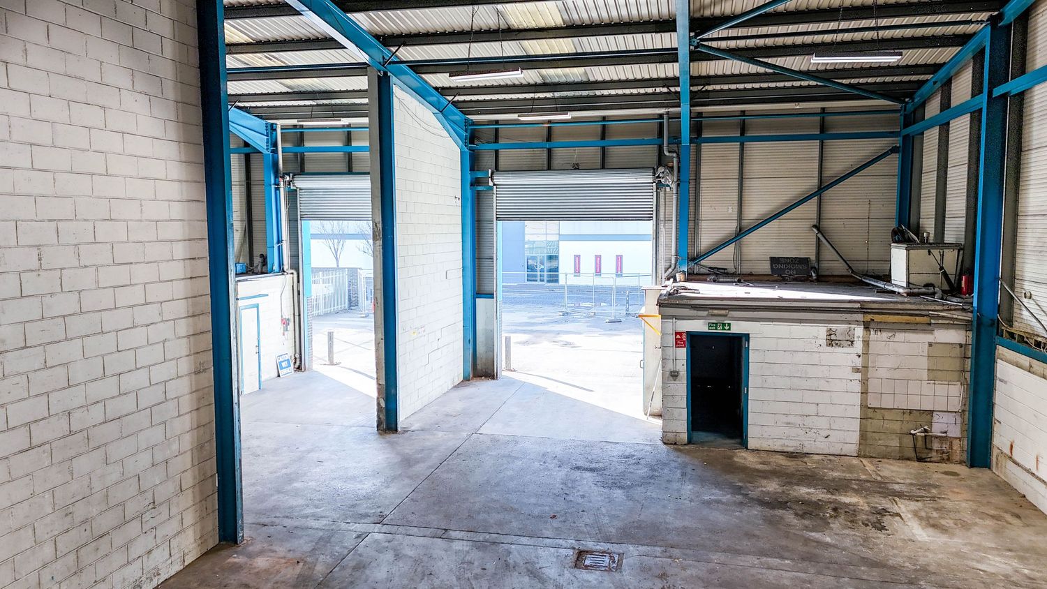 Interior panorama of an empty warehouse space with white walls and blue support beams.