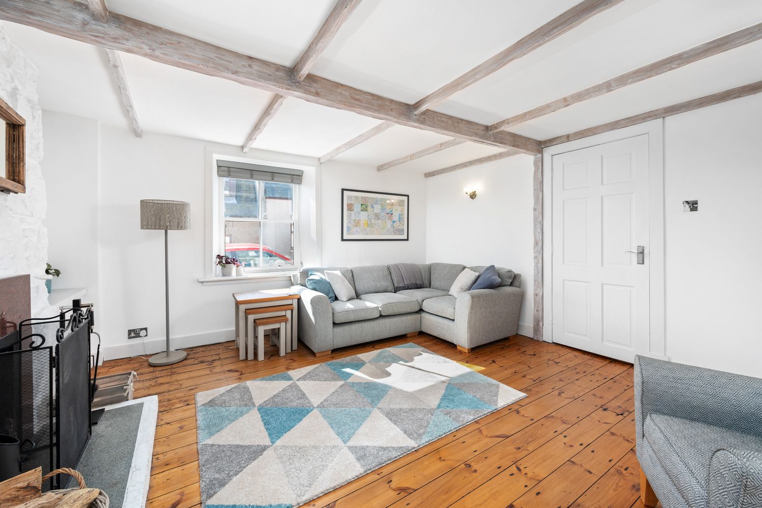 Modern living room with wood floors, exposed beams, grey sectional sofa, geometric area rug and natural lighting.