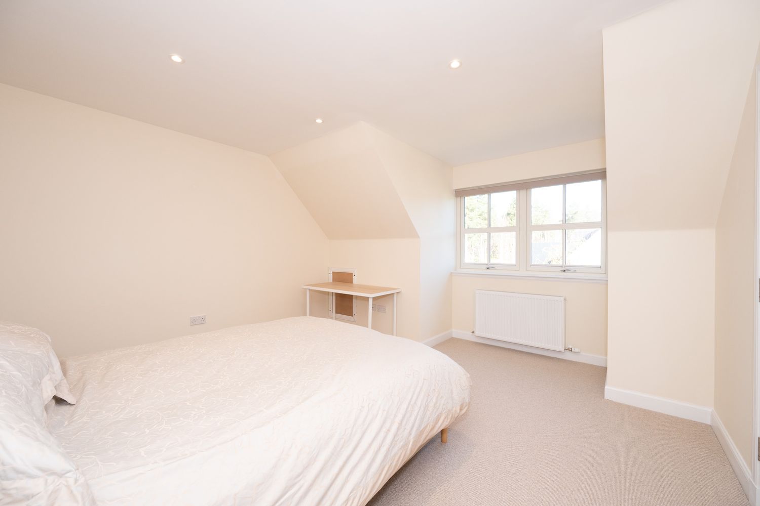Bright and minimalist loft bedroom with white walls, beige carpet, and a large window offering natural light.