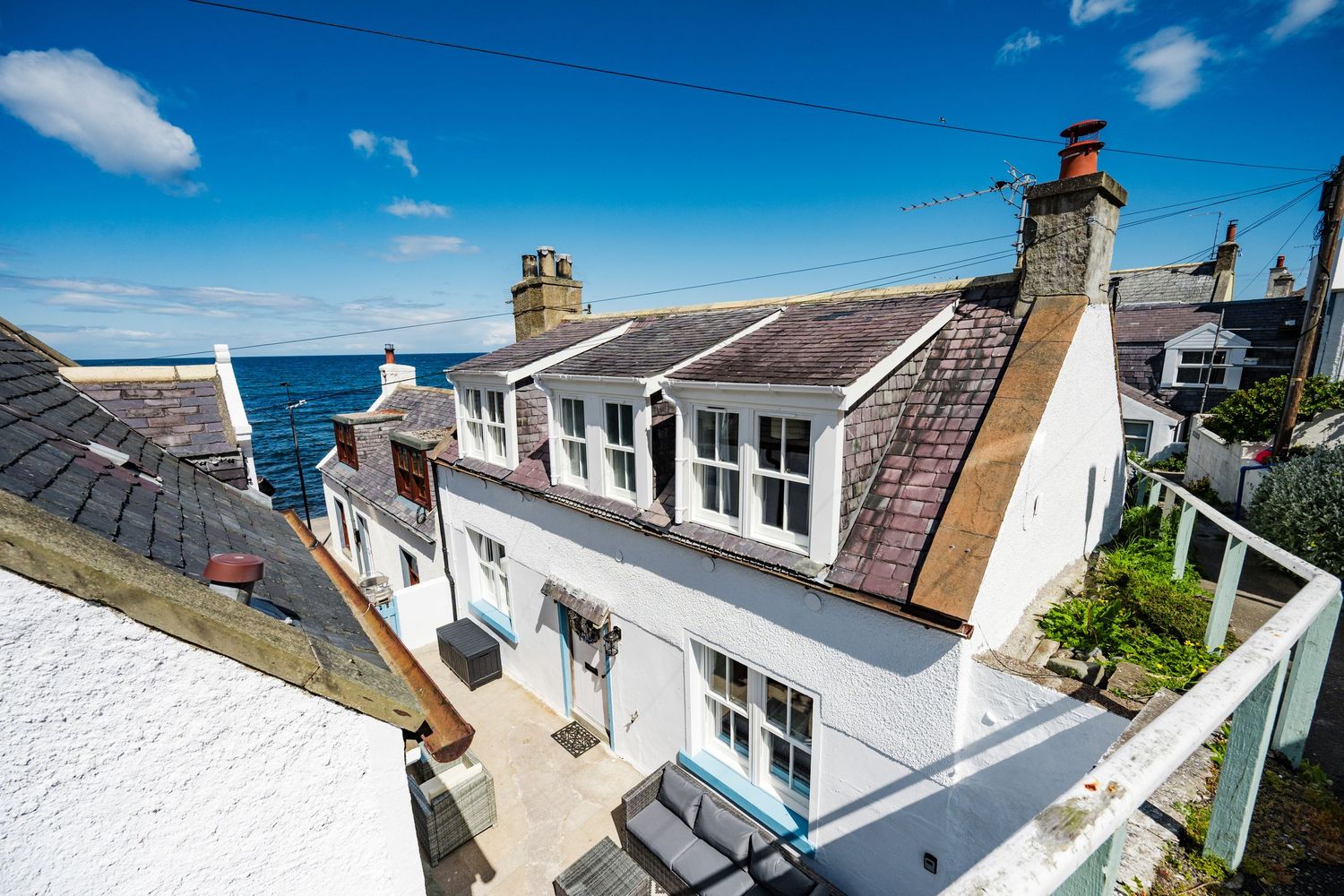 Aerial view of white coastal cottage with dormer windows and chimneys overlooking the ocean.