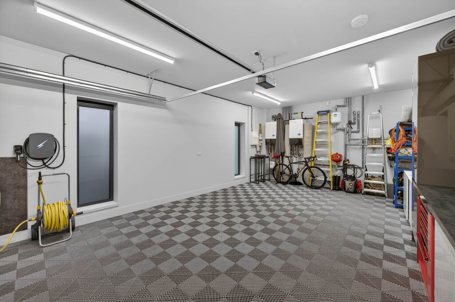 Modern garage interior with white walls, checkered floor tiles, and bright fluorescent lighting along the ceiling.