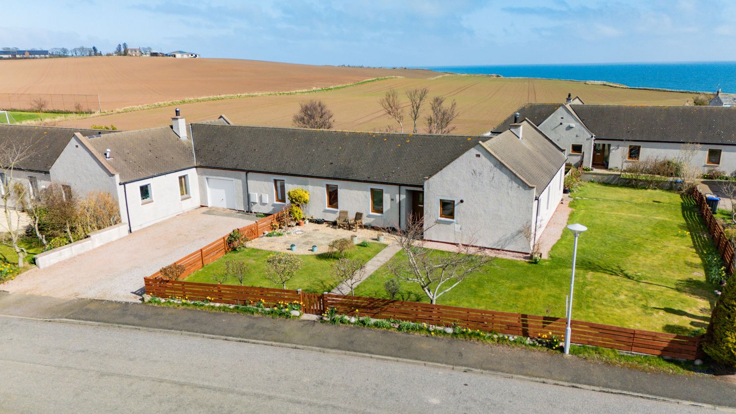 Aerial view of white bungalow home with manicured garden and driveway overlooking coastal scenery in Scotland.