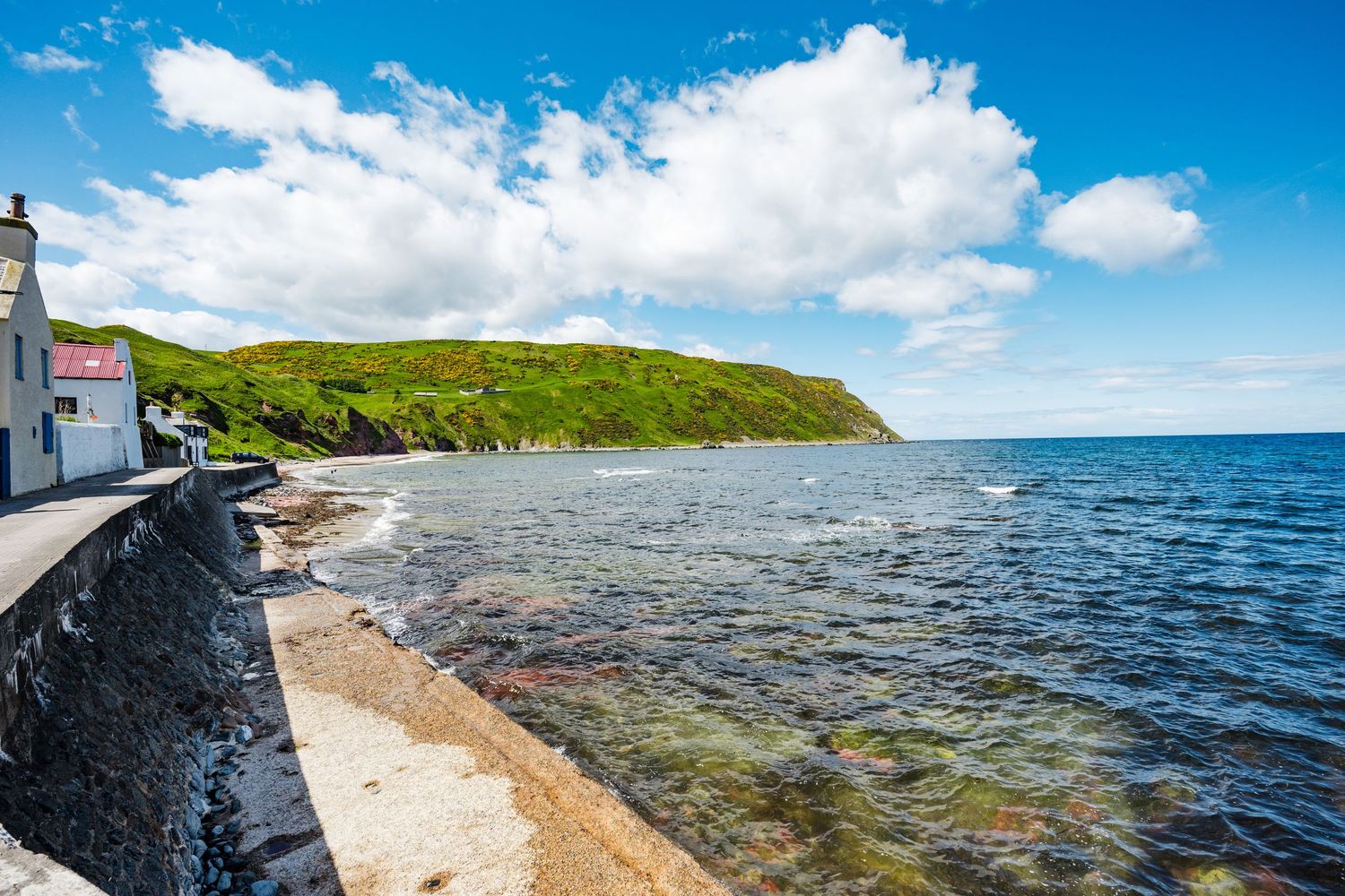 Scenic coastline with white buildings overlooking clear blue waters and rocky shores under bright sky.