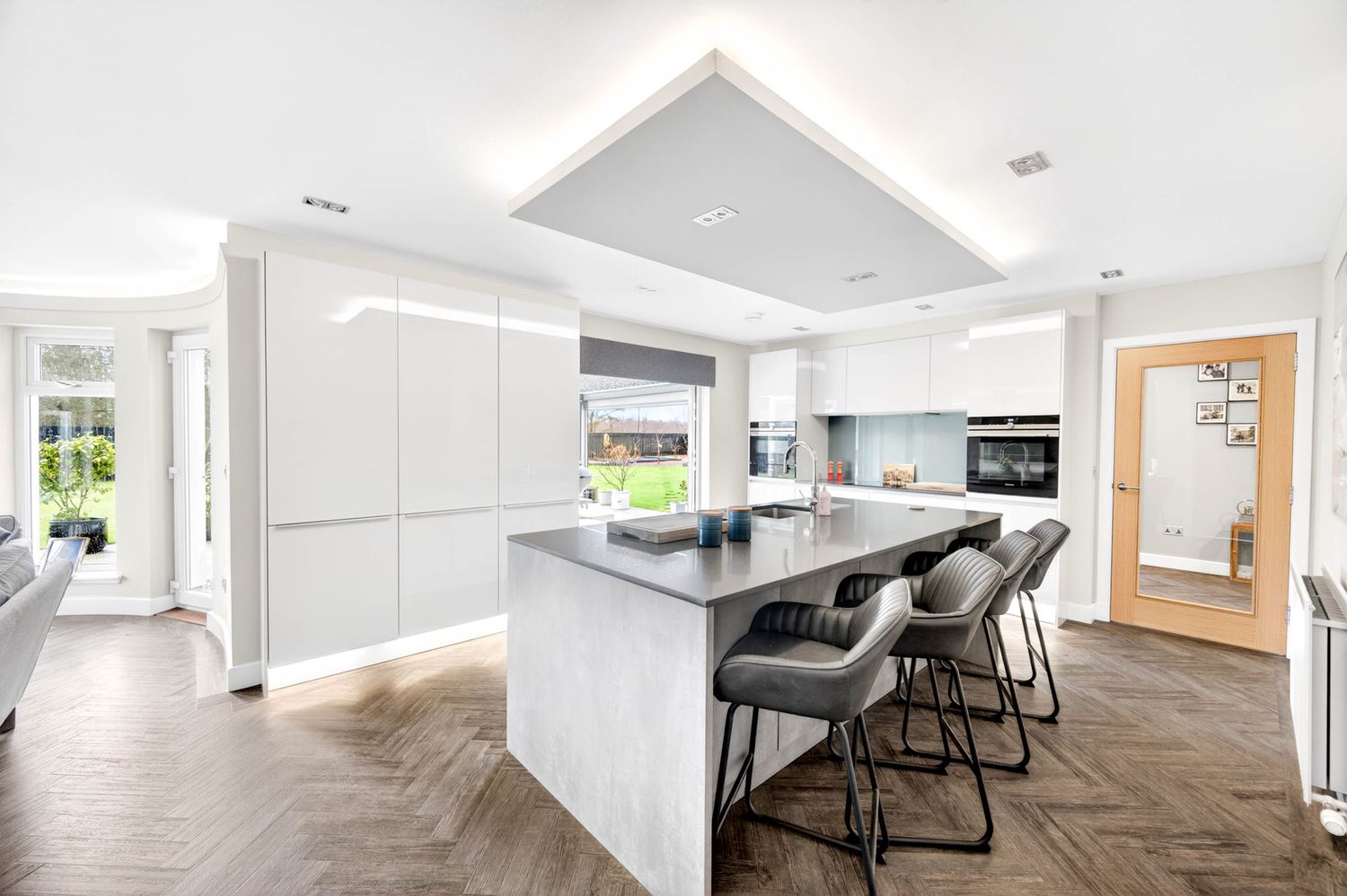 Modern white kitchen featuring herringbone flooring, sleek cabinetry, and a large center island with bar seating.