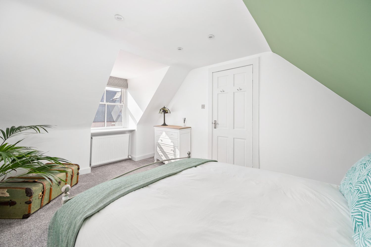 Minimalist attic bedroom with white walls, green accent wall and turquoise bedding.