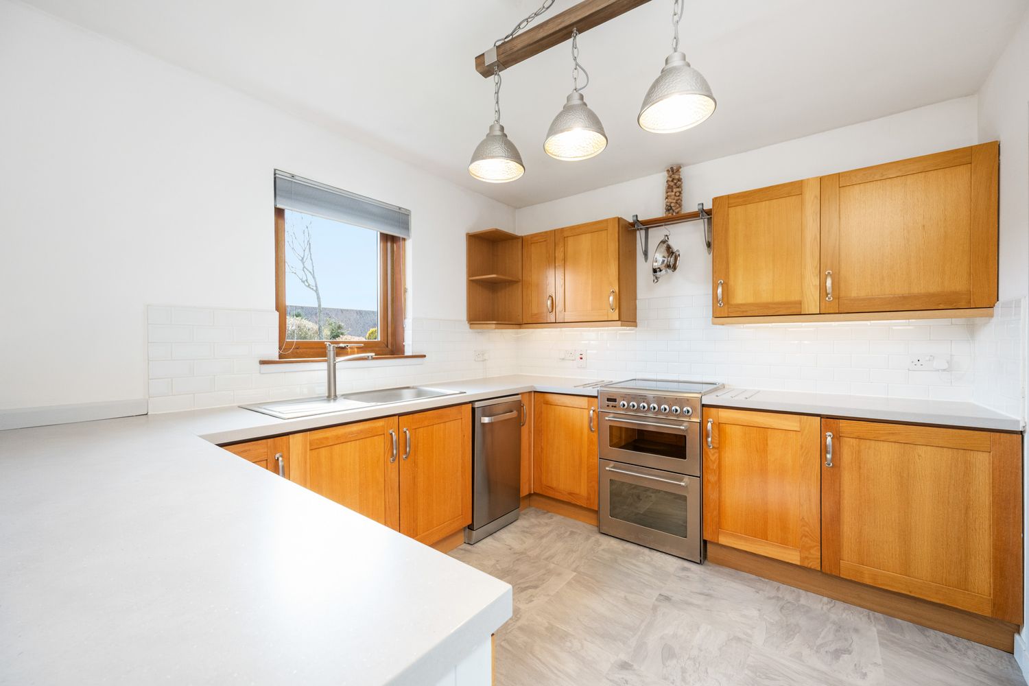 Modern L-shaped kitchen with honey oak cabinets, white countertops, stainless steel appliances and pendant lighting.