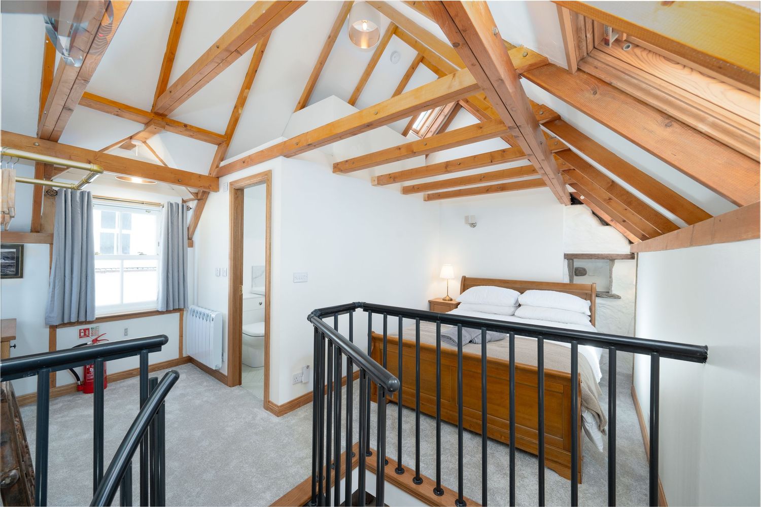 Modern loft space with exposed wooden beams, white walls, and black metal railing leading to an upper level.