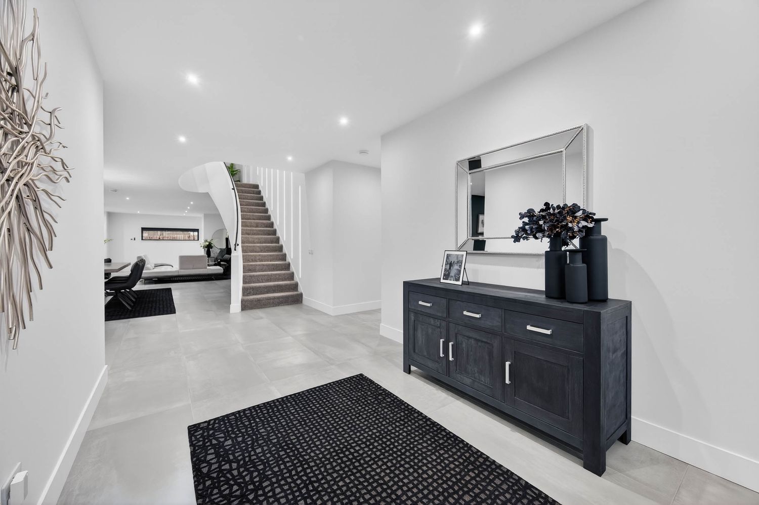Modern white hallway with recessed lighting, black and white decor, and hardwood flooring leads to an elegant staircase.