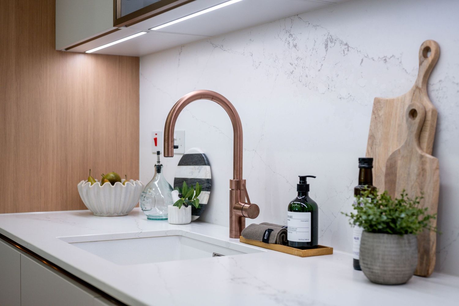 Modern kitchen counter with copper faucet, white marble surface, and decorative wooden accessories.