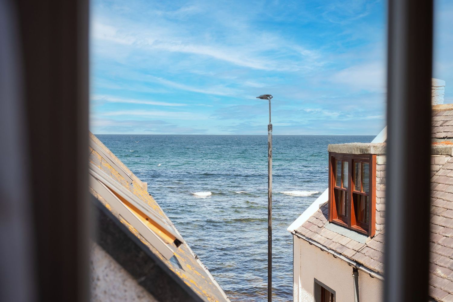 Scenic ocean view between buildings showing blue sky and a street lamp against the sea horizon.