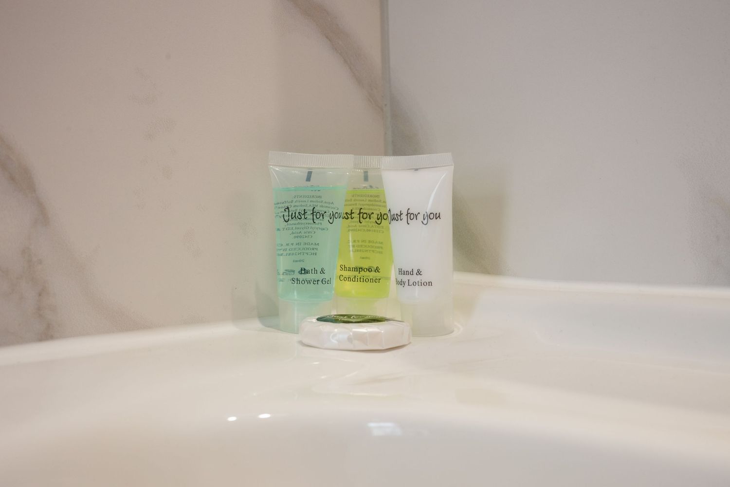 Hotel bathroom amenities with small toiletry bottles displayed on white marble countertop.